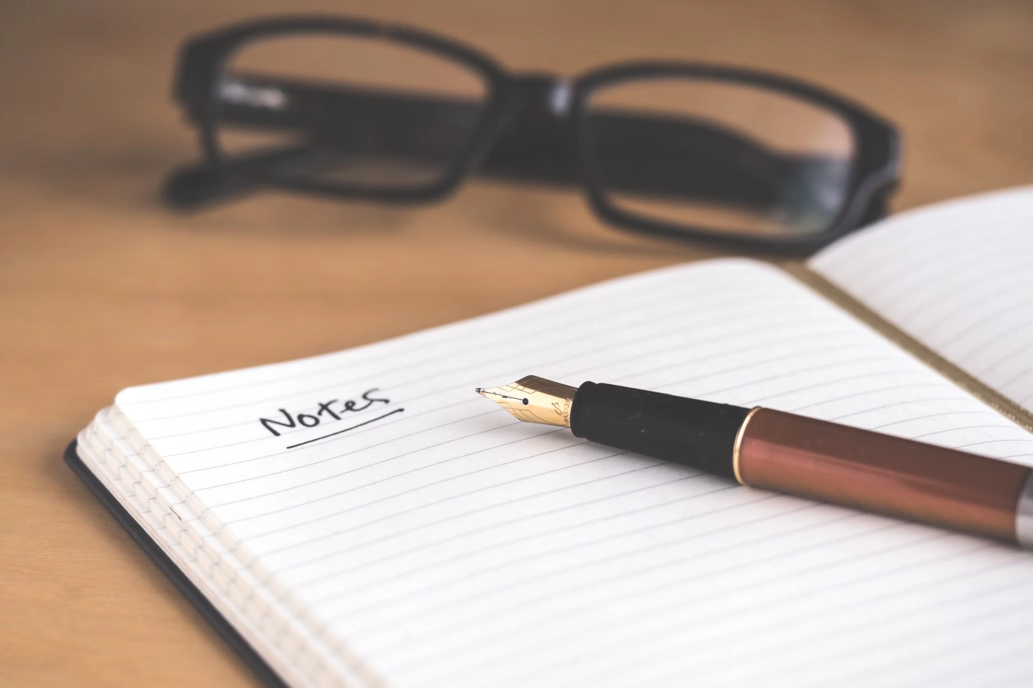 caderno com caneta e óculos em cima de uma mesa