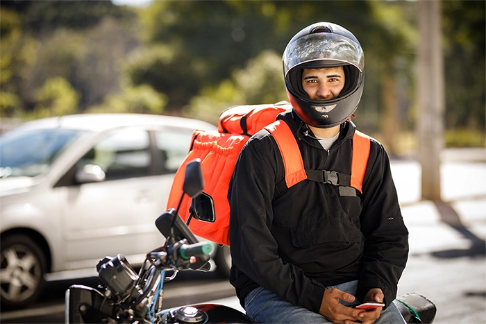 motoboy de capacete com mochila encostado em uma moto